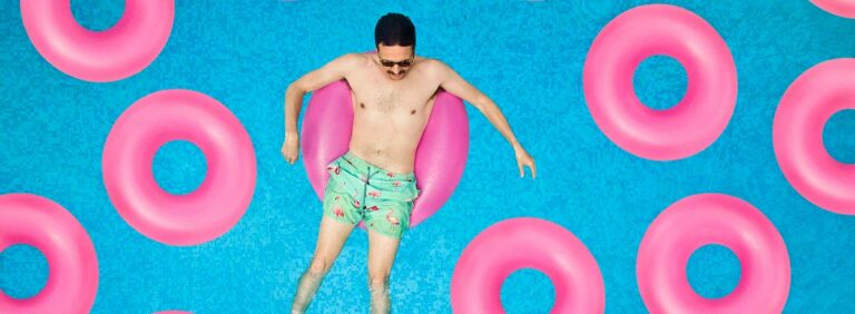 man floating in pink plastic ring in a pool